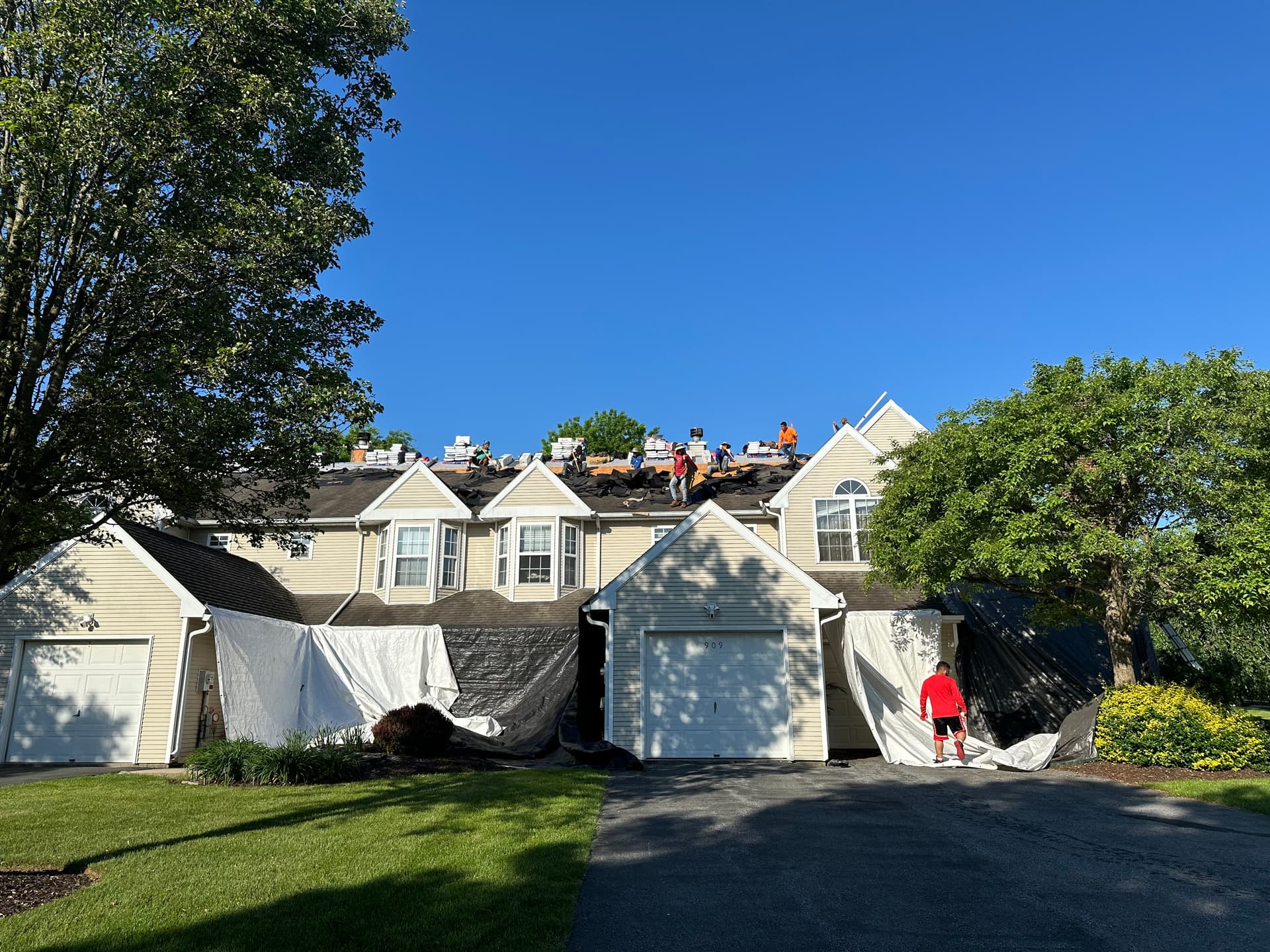 E&K crew mid-roof-replacement on a row of townhomes, with tarps protecting the siding and landscaping below
